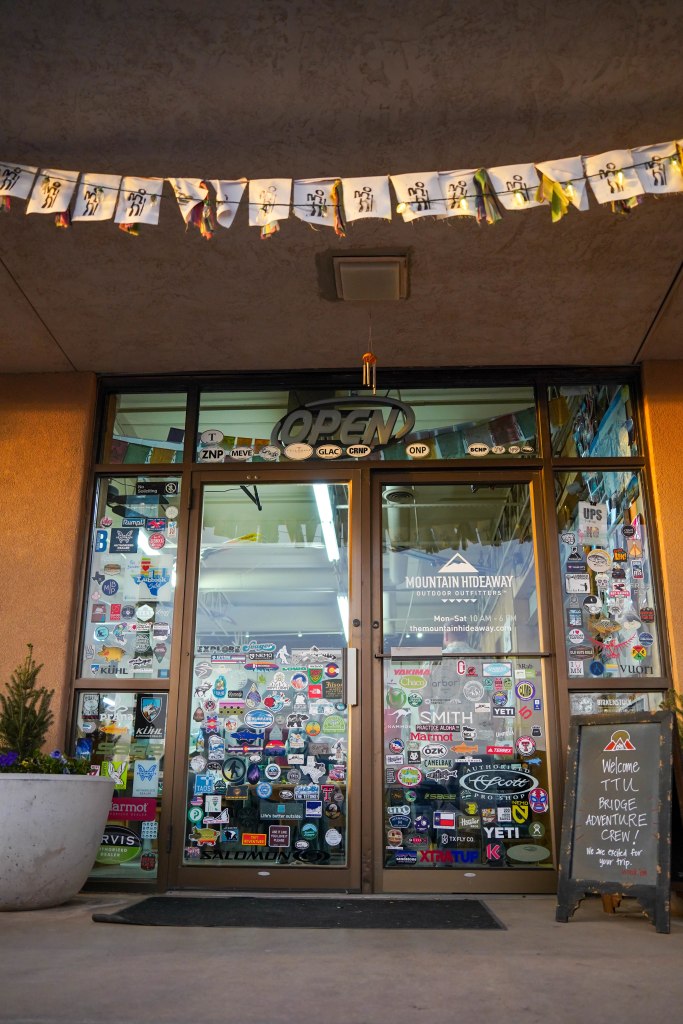 Entrance of Mountain Hideaway outdoor outfitters with an open sign and various stickers displayed on glass doors.