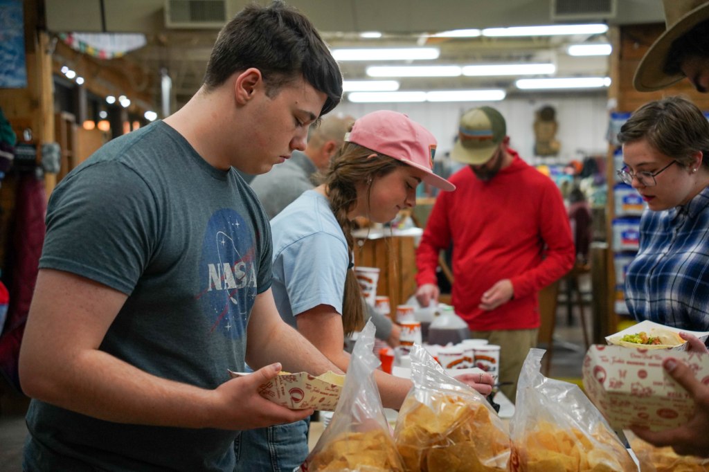 Students participating in Bridge Adventure self-serving food at a communal dining area, with various food items visible in the foreground.