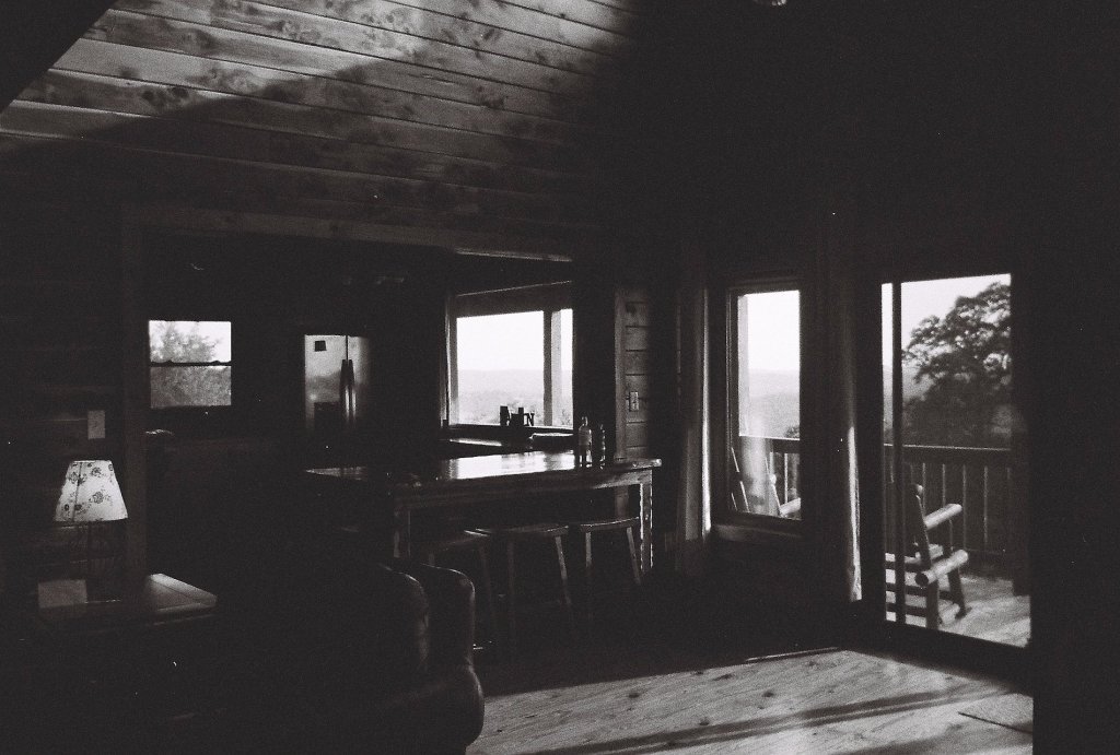 Interior of a rustic cabin with wooden walls, featuring a bar area and a view through large windows.