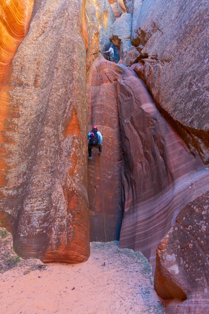 A person rappelling down a steep sandstone wall inside a slot canyon, showcasing the unique geological formations and textures of the rock.